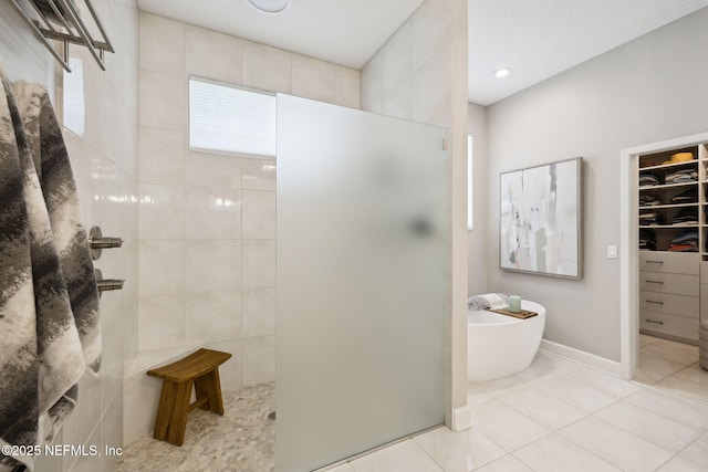 bathroom with baseboards, tile patterned floors, a spacious closet, walk in shower, and a freestanding bath