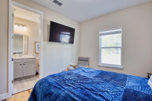 bedroom featuring ensuite bathroom, sink, light hardwood / wood-style flooring, and a textured ceiling