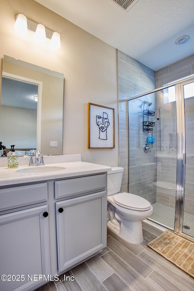 bathroom featuring an enclosed shower, vanity, a textured ceiling, and toilet