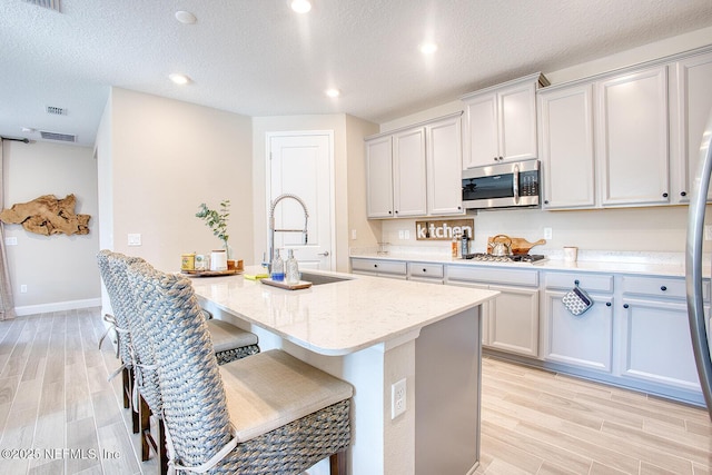 kitchen with sink, a breakfast bar area, appliances with stainless steel finishes, a kitchen island with sink, and light stone countertops