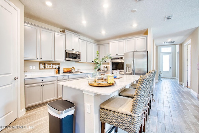 kitchen featuring a breakfast bar, stainless steel appliances, light stone counters, a textured ceiling, and a kitchen island