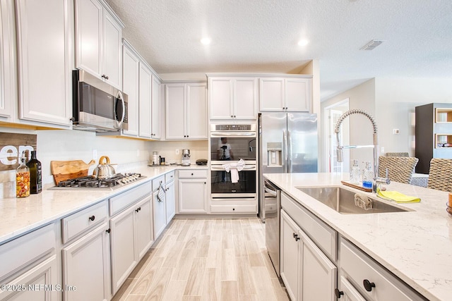 kitchen featuring sink, light wood-type flooring, stainless steel appliances, light stone countertops, and white cabinets