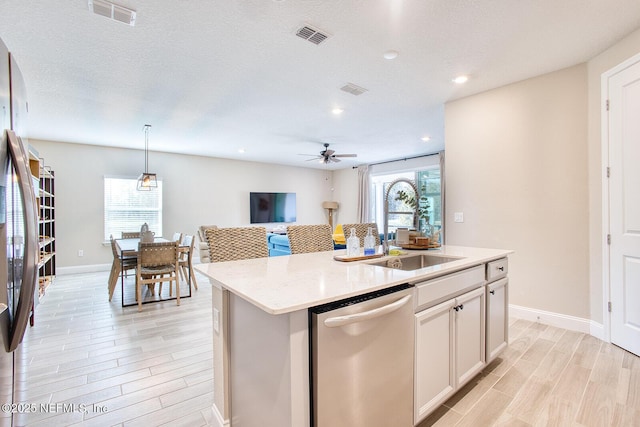 kitchen featuring appliances with stainless steel finishes, decorative light fixtures, an island with sink, sink, and white cabinets