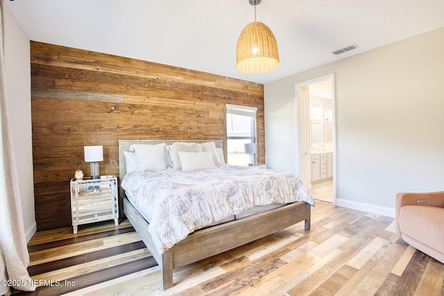 bedroom featuring connected bathroom, wooden walls, and hardwood / wood-style floors