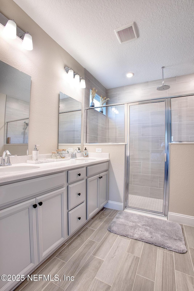 bathroom with a shower with door, vanity, and a textured ceiling