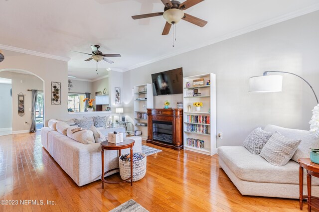 living room with arched walkways, baseboards, ornamental molding, light wood-type flooring, and a glass covered fireplace