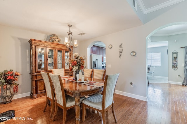 dining room with arched walkways, light wood-style flooring, visible vents, and a notable chandelier