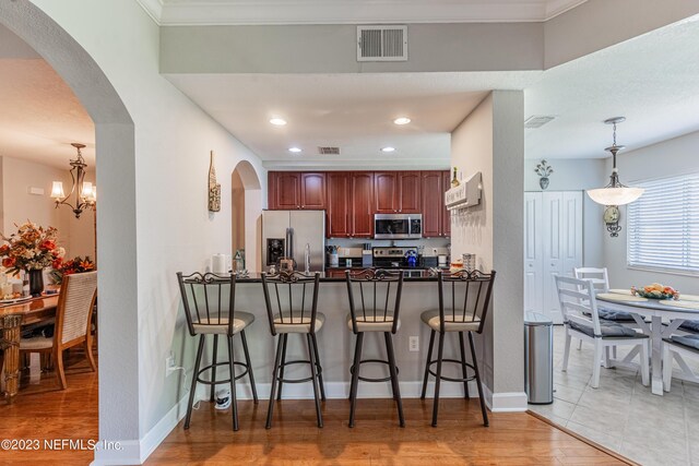 kitchen featuring visible vents, dark countertops, a breakfast bar, hanging light fixtures, and stainless steel appliances