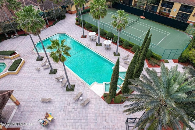 community pool featuring a tennis court, a patio area, and fence