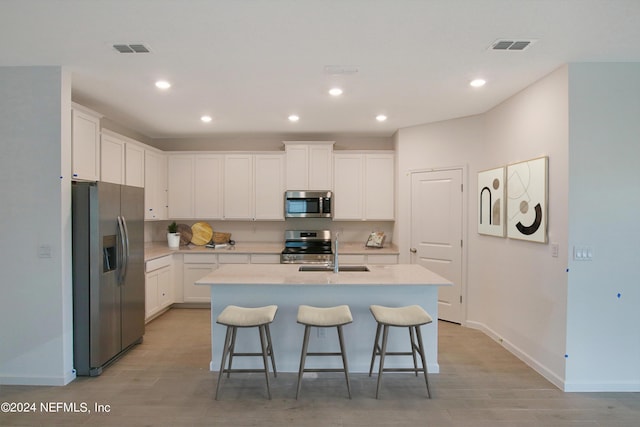 kitchen with a kitchen bar, sink, appliances with stainless steel finishes, a kitchen island with sink, and white cabinets