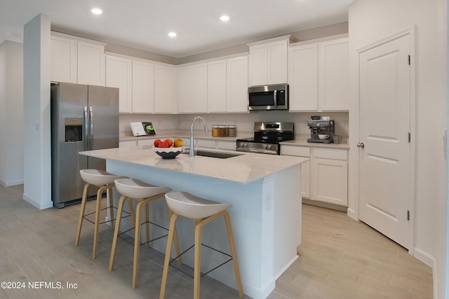 kitchen with sink, a breakfast bar area, white cabinetry, stainless steel appliances, and an island with sink