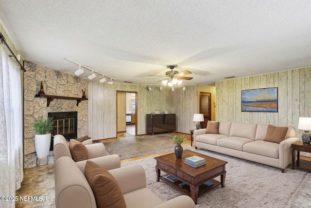 living area featuring visible vents, a ceiling fan, a textured ceiling, and a stone fireplace