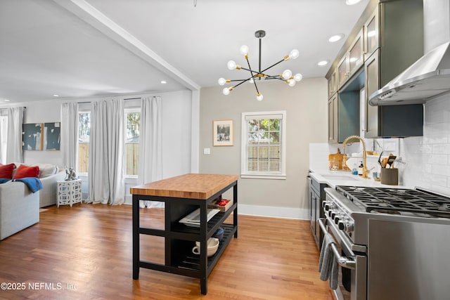 kitchen featuring decorative backsplash, green cabinets, stainless steel range, light hardwood / wood-style floors, and wall chimney exhaust hood