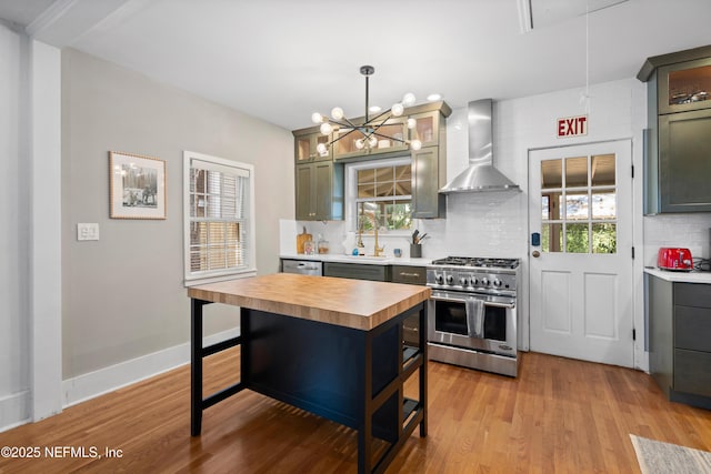 kitchen featuring tasteful backsplash, wall chimney exhaust hood, decorative light fixtures, and high end stove