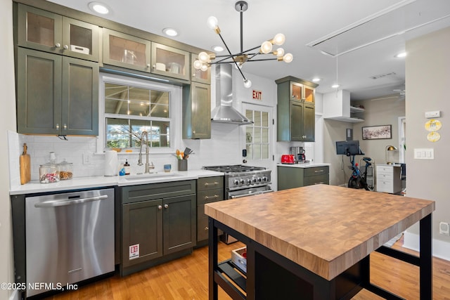 kitchen featuring stainless steel appliances, sink, hanging light fixtures, and wall chimney range hood