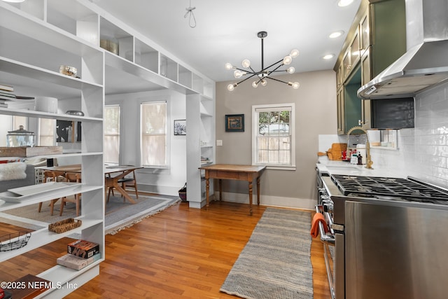 kitchen with sink, green cabinets, high end stainless steel range, wall chimney range hood, and light hardwood / wood-style flooring