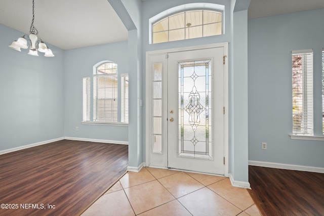 tiled foyer with arched walkways, an inviting chandelier, and baseboards