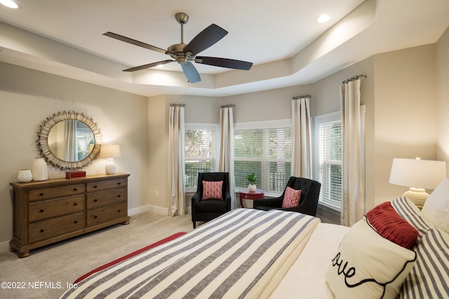 bedroom featuring a tray ceiling, light colored carpet, and ceiling fan