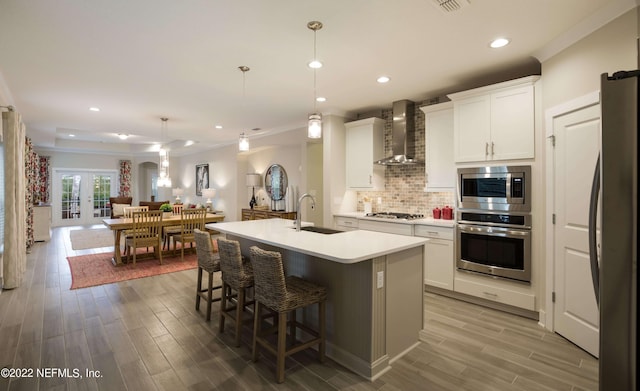 kitchen featuring sink, white cabinetry, stainless steel appliances, an island with sink, and wall chimney exhaust hood