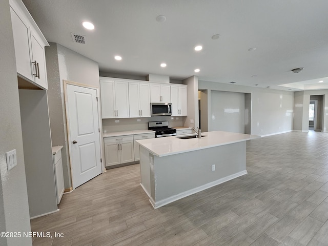 kitchen featuring sink, appliances with stainless steel finishes, light hardwood / wood-style floors, white cabinets, and a center island with sink