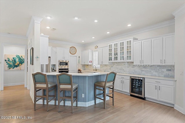 kitchen featuring wine cooler, a breakfast bar, white cabinets, light countertops, and appliances with stainless steel finishes