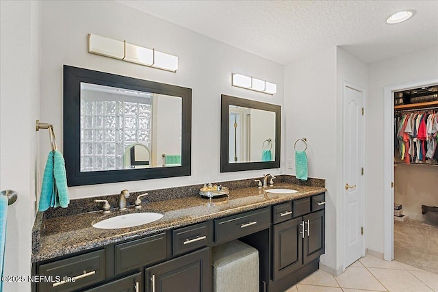 full bath with a textured ceiling, a sink, tile patterned floors, double vanity, and a walk in closet