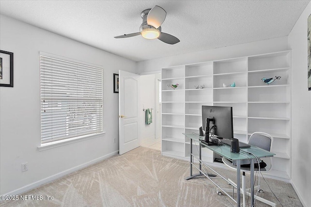 office featuring ceiling fan, a textured ceiling, baseboards, and light colored carpet