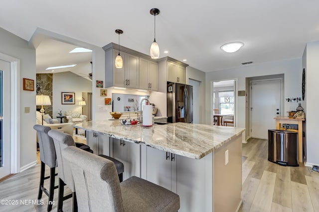 kitchen featuring gray cabinetry, light wood-type flooring, refrigerator with ice dispenser, pendant lighting, and light stone countertops