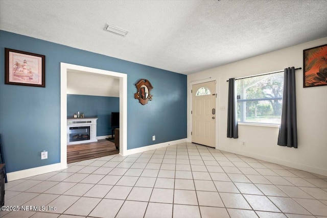 foyer entrance with light tile patterned floors, baseboards, visible vents, a textured ceiling, and a fireplace