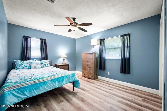 bedroom featuring a textured ceiling, multiple windows, light wood-style flooring, and baseboards