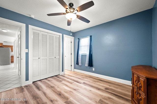 unfurnished bedroom featuring light wood-type flooring, freestanding refrigerator, a closet, and baseboards