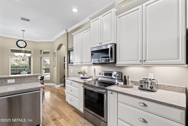 kitchen with stainless steel appliances, ornamental molding, white cabinets, and light stone counters