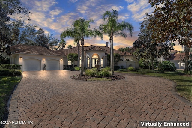 mediterranean / spanish house with a garage, decorative driveway, a tile roof, and stucco siding