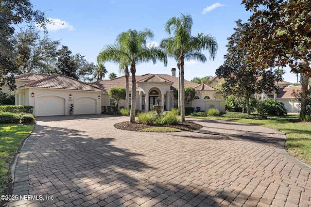 mediterranean / spanish house with a garage, decorative driveway, and stucco siding