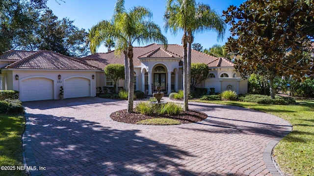 mediterranean / spanish house featuring an attached garage, a tiled roof, french doors, stucco siding, and curved driveway