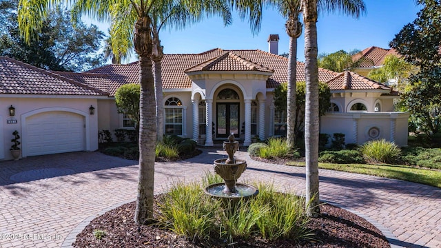 mediterranean / spanish home with an attached garage, a tiled roof, french doors, decorative driveway, and stucco siding