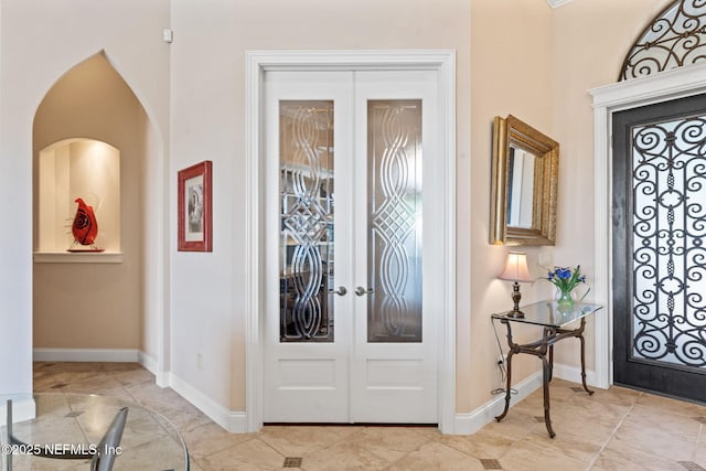 foyer featuring arched walkways, french doors, and baseboards