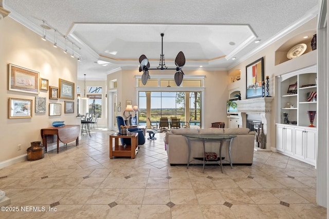 living room featuring baseboards, a glass covered fireplace, a tray ceiling, a textured ceiling, and crown molding