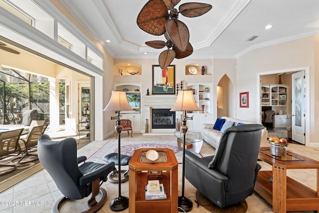 living room featuring built in features, arched walkways, ornamental molding, a ceiling fan, and a large fireplace