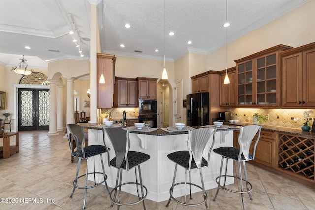 kitchen with arched walkways, black appliances, a kitchen bar, and decorative columns