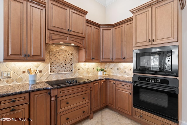 kitchen with black appliances, tasteful backsplash, brown cabinetry, and dark stone countertops