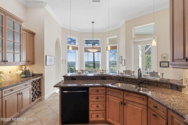 kitchen with dishwasher, brown cabinetry, dark stone counters, and a sink