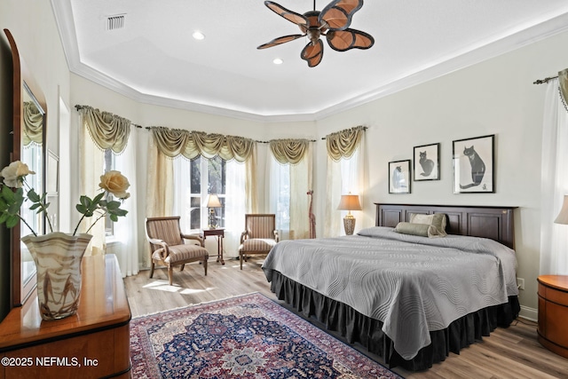 bedroom with a raised ceiling, wood finished floors, visible vents, and crown molding