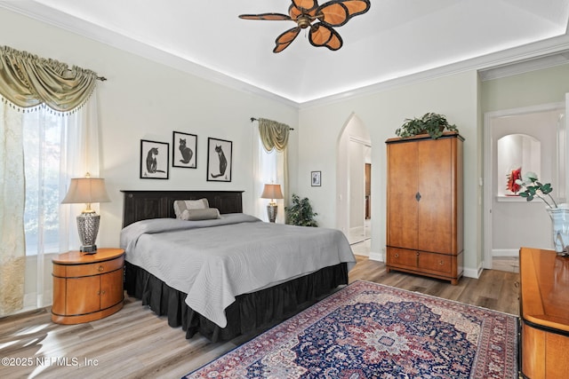 bedroom featuring arched walkways, crown molding, a raised ceiling, wood finished floors, and baseboards