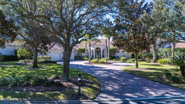 mediterranean / spanish home with a garage, decorative driveway, a tiled roof, and a front lawn