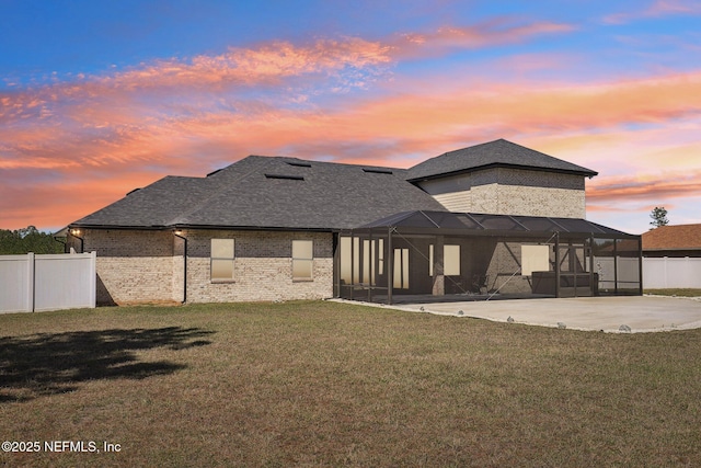 rear view of property with brick siding, a patio, a lawn, glass enclosure, and fence