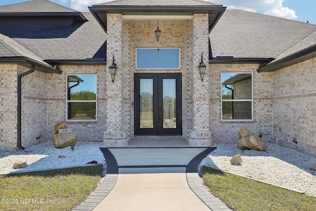 entrance to property with french doors, brick siding, and a shingled roof