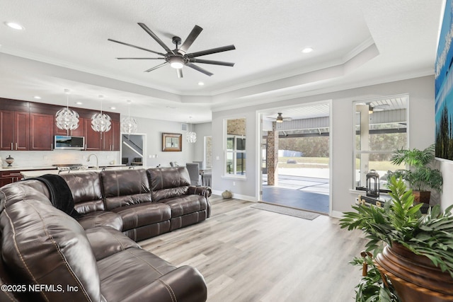 living area featuring a raised ceiling, crown molding, light wood-style flooring, and ceiling fan