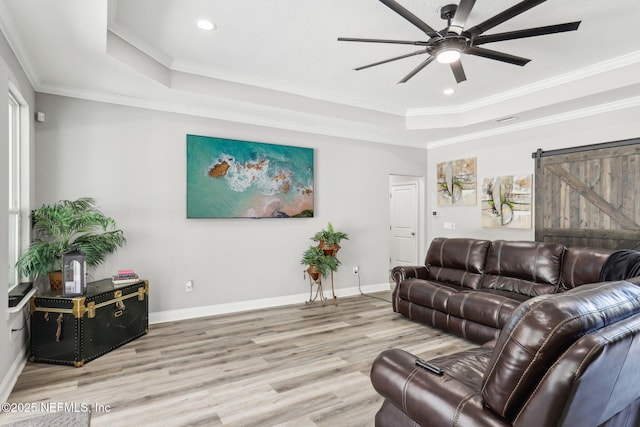 living area with a tray ceiling, a barn door, wood finished floors, and crown molding