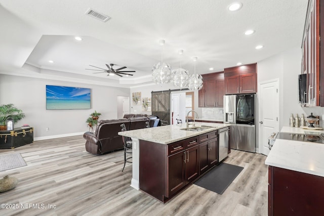 kitchen with stainless steel appliances, a raised ceiling, visible vents, a barn door, and a sink